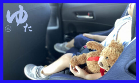 チャイルドシートのうえで眠る子どもの横に熊の人形