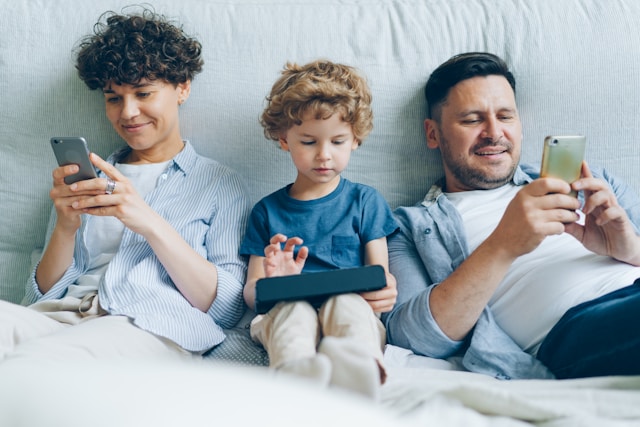 スマホを見ている両親と、タブレットを見ている子ども