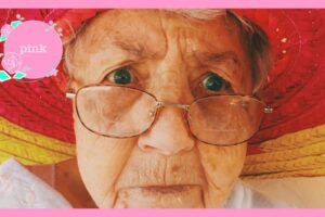 黄色の縁取りのアイ会麦わら帽子を被っている、眼鏡をかけたおばあさん