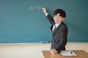 黒板の前でチョークを持ち、教えるスーツの男性