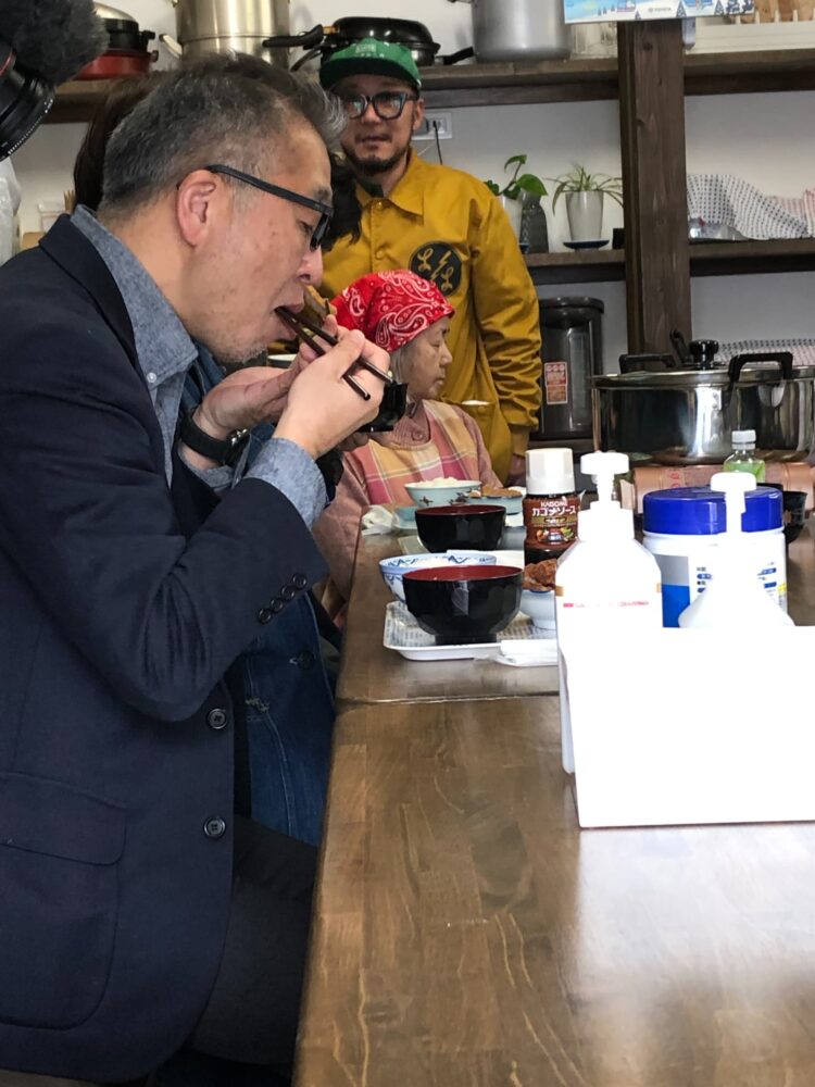 ご飯を並んで食べる人々と見守る男性