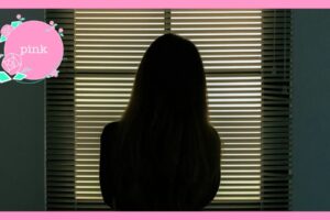 ブラインドの外を見ているロングヘアの女性の後ろ姿