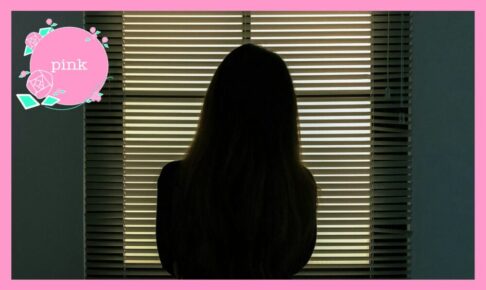ブラインドの外を見ているロングヘアの女性の後ろ姿