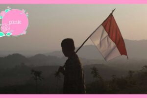 インドネシアの国旗を手に持ち肩に担いで、山々を見ている男性