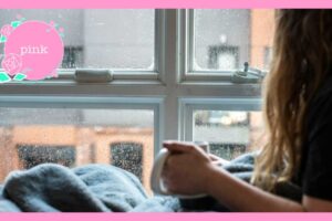 マグカップを手に持ち、雨が降っている窓の外を見ている女性
