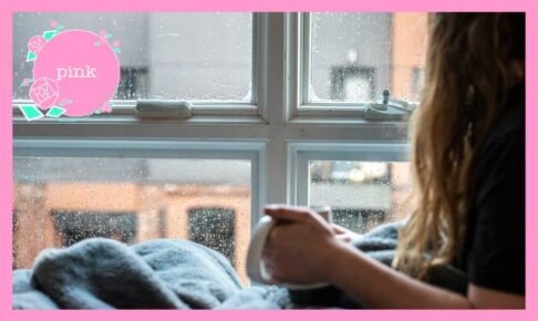 マグカップを手に持ち、雨が降っている窓の外を見ている女性