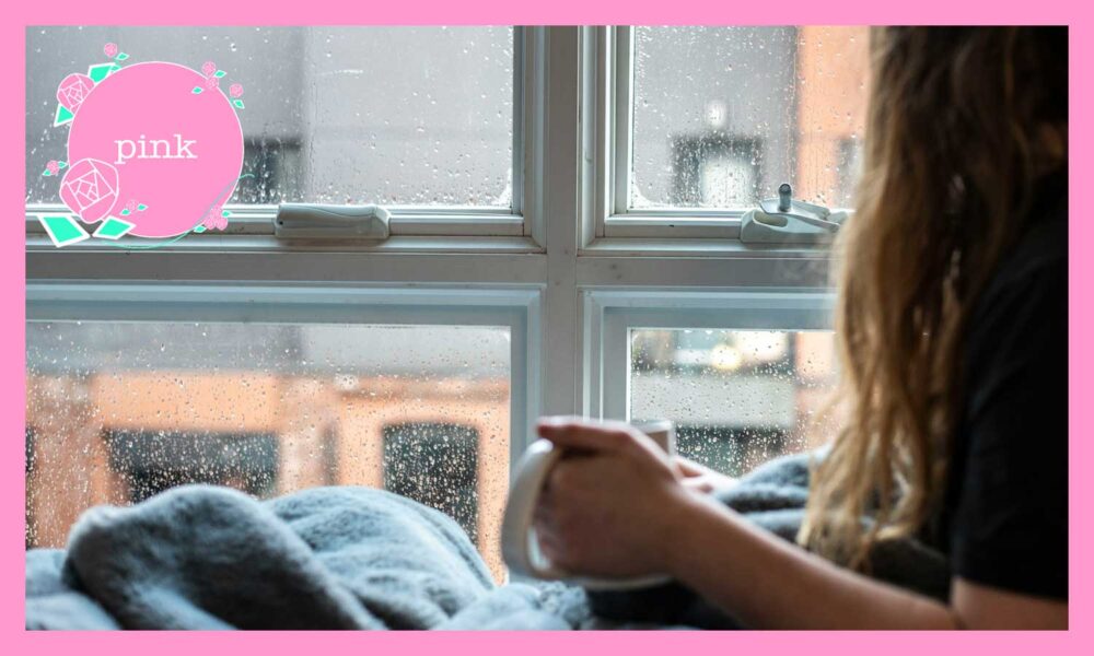 マグカップを手に持ち、雨が降っている窓の外を見ている女性