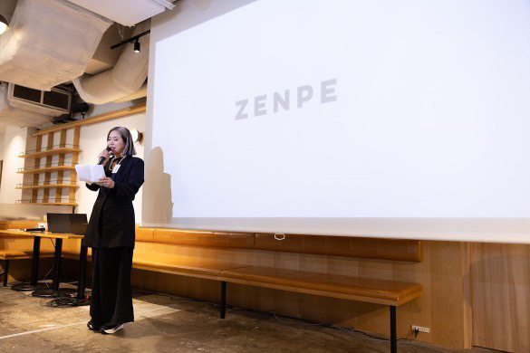 『ZENPE』の文字が浮かぶスクリーンで、講演する女性