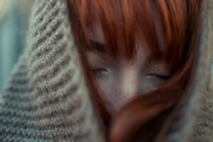 グレーのニットで頭を覆い、目を閉じている茶色い髪の女性