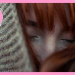 グレーのニットで頭を覆い、目を閉じている茶色い髪の毛の女性
