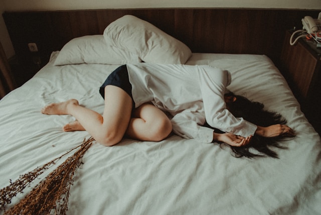 両手で顔を隠して、ベットにうずくまる女性