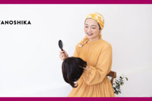 外したウィッグを手に持っているオレンジの服を着た女性
