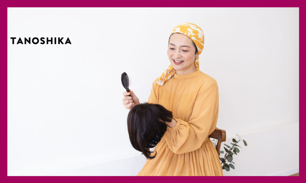 外したウィッグを手に持っているオレンジの服を着た女性