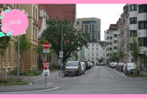 周りを高いビルに囲まれている場所、駐車した車が並んでいる通り。