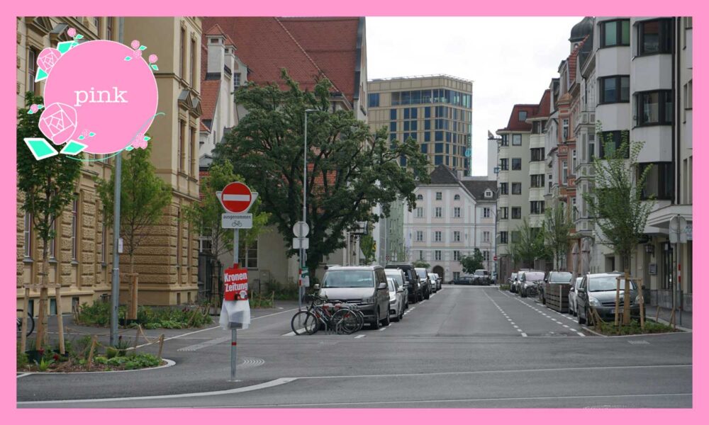 周りを高いビルに囲まれている場所、駐車した車が並んでいる通り。