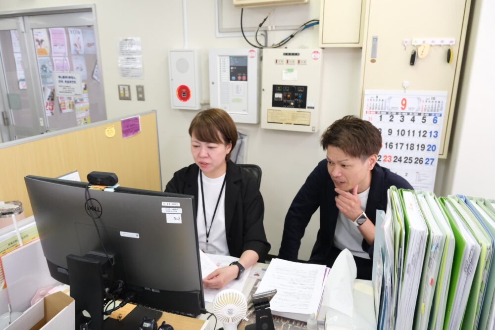 久保田さんと林さんが並んで机に座って仕事の話をしている