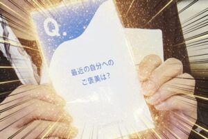 「最近の自分へのご褒美は？」と書かれたカードを両手で持っている