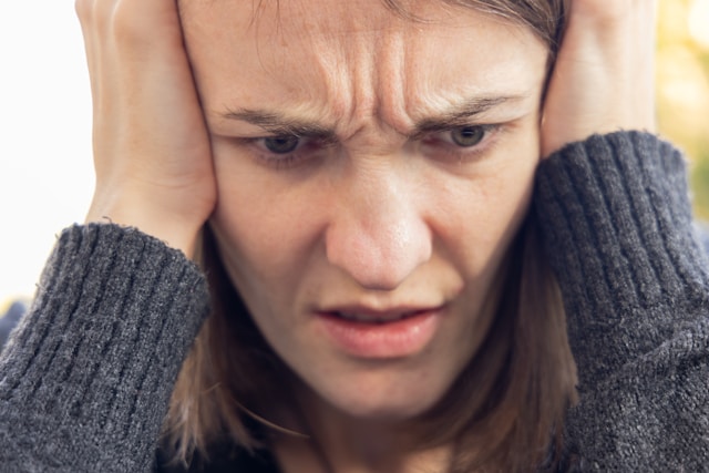こめかみを両手で押さえ、つらい表情の女性