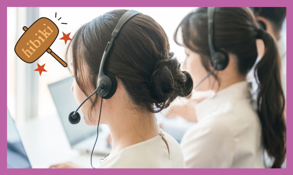 コールセンタで、女性や男性がヘッドホンとマイクが一緒になったヘッドセットをつけ、お客様とパソコン画面を見ながら話している。