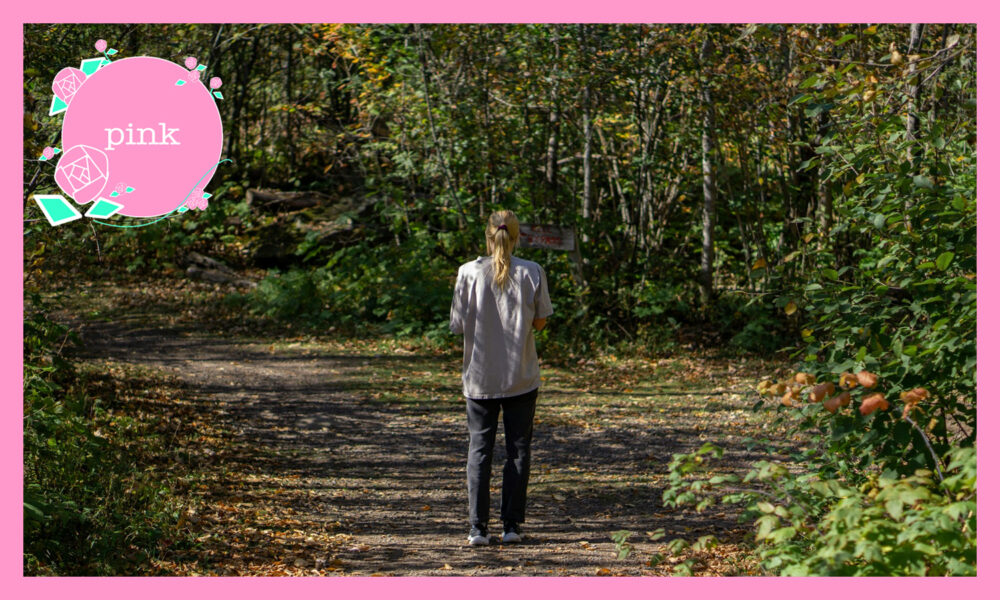 森の中、金髪をポニーテールにして、グレーのTシャツにジーンズ姿の女性の後ろ姿