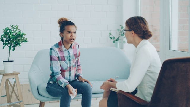 ソファに座り、眼鏡をかけた女性と向き合い、カウンセリングを受けている少女