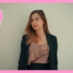 スーツを着て、壁の前に立っている、髪の長い女性