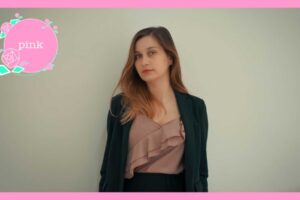スーツを着て、壁の前に立っている、髪の長い女性