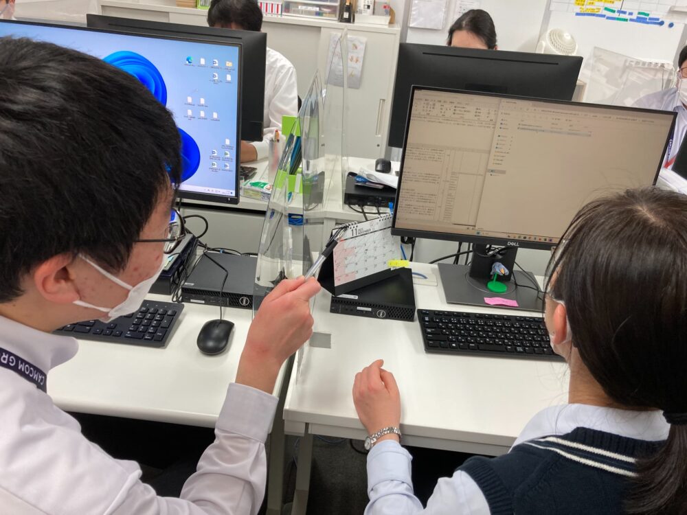 オフィスでPC業務について男性からサポートを受ける女性