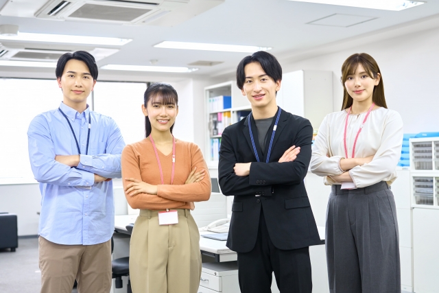 腕を組んだ4人の男女が微笑んで職場にいる光景。