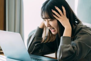 パソコンを観た女性が、頭を抱えて悩んでいる。

