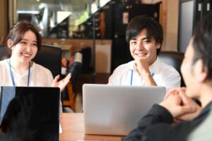 3~4人の男女が向かい合って、パソコンを開けて打ち合わせしている。