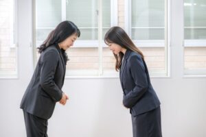 スーツを着た女性二人が、にこやかに挨拶している。