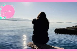 岩の上にすわり、海を眺めている女性の後ろ姿