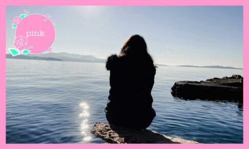 岩の上にすわり、海を眺めている女性の後ろ姿
