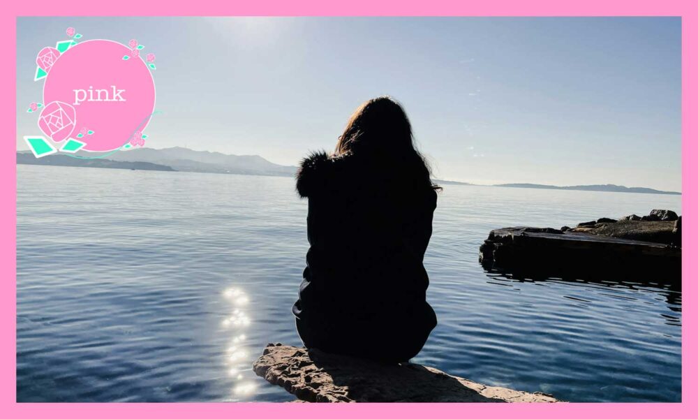 岩の上にすわり、海を眺めている女性の後ろ姿