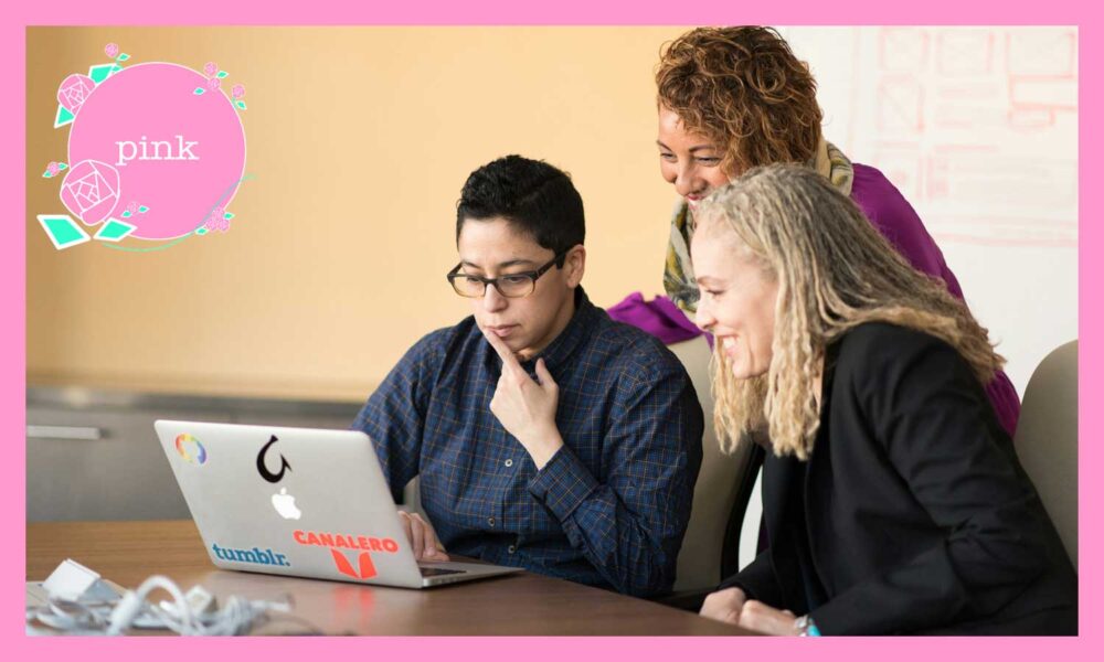 机に座ってノートパソコンを見ている眼鏡の男性と、隣にいる2人の女性