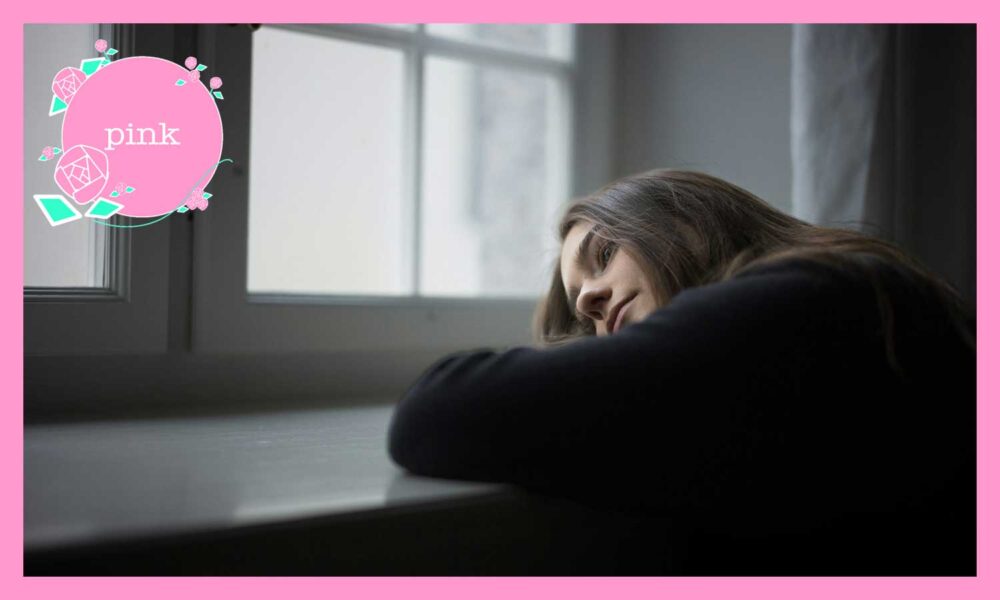 窓辺のテーブルに腕を置き、頬を預けながら外をぼんやり見つめる女性