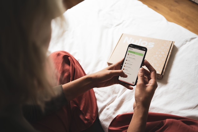 ベッドの上に座り、スマートフォンを操作している女性