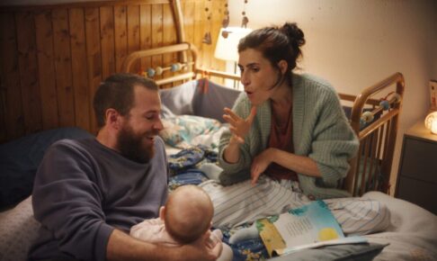 ベッドの上で、手話をつかって子どもをあやす女性と、子どもを支える男性