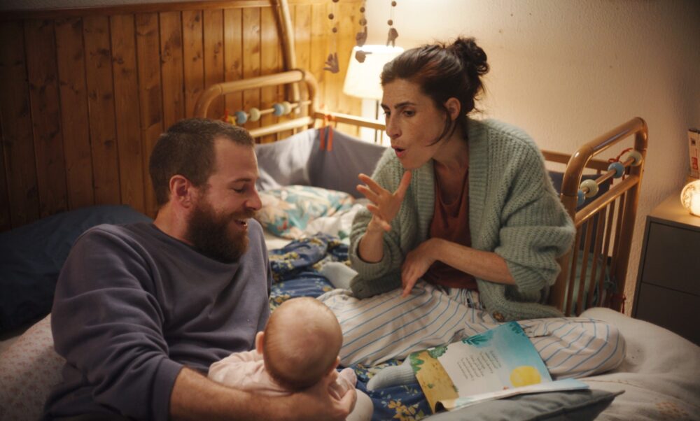 ベッドの上で、手話をつかって子どもをあやす女性と、子どもを支える男性
