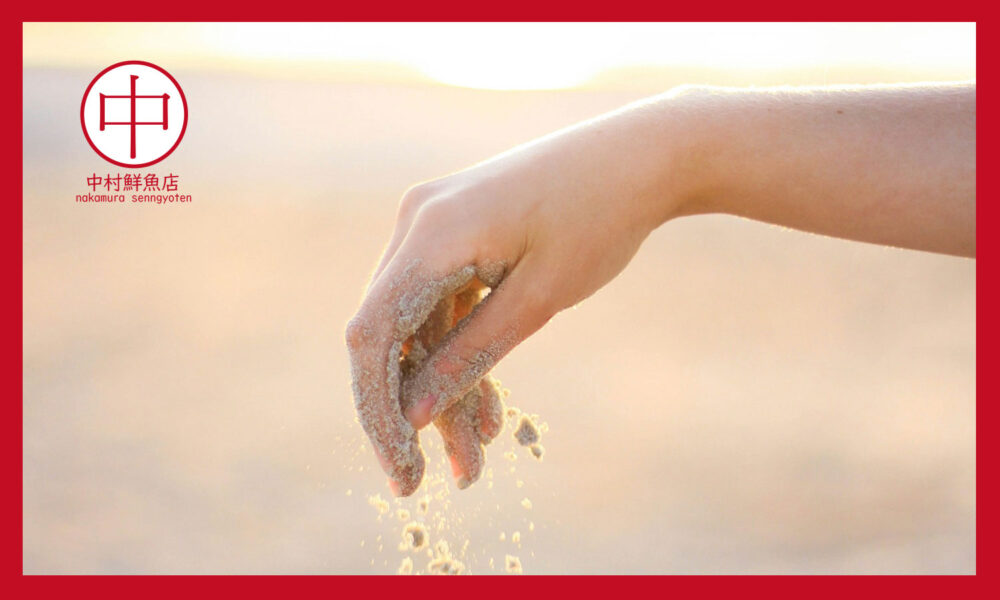 夕日の浜辺で砂をこぼす手