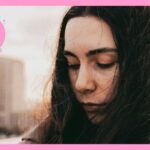 都会の屋外で、風に髪をなびかせながら目を閉じて静かにたたずむ女性