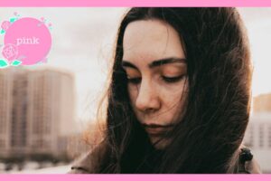都会の屋外で、風に髪をなびかせながら目を閉じて静かにたたずむ女性