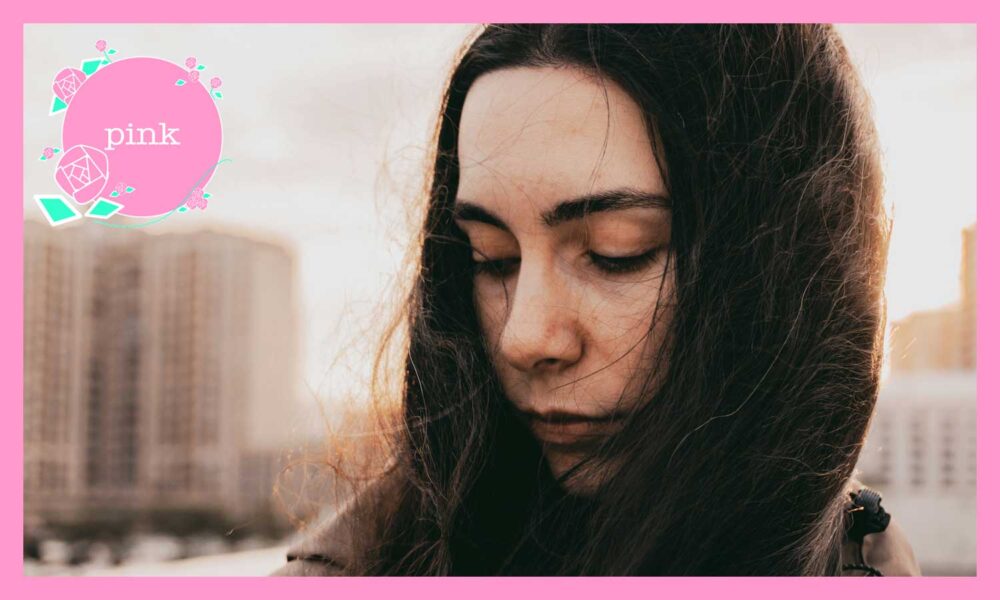 都会の屋外で、風に髪をなびかせながら目を閉じて静かにたたずむ女性