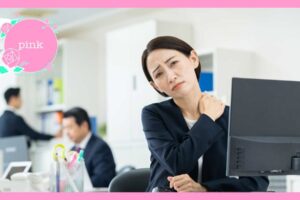 オフィスのデスクに座り、肩に手を当てて痛そうにしている女性