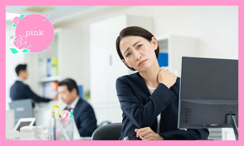 オフィスのデスクに座り、肩に手を当てて痛そうにしている女性