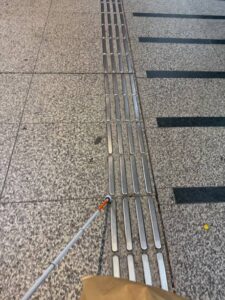 画面中央を縦に、金属製の突起がある線状の点字ブロックがまっすぐ延びている。白杖がそれを使用している場面