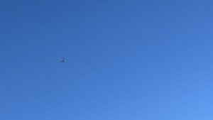 真っ青な明るい空に一機の飛行機が左端で飛んでいる