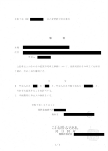 令和7年の「名の変更許可申立事件」における福岡家庭裁判所の審判書（謄本）。「主文」の1番に、申立人の名および名の振り仮名の変更を許可する旨、2番に手続き費用は申立人の負担とする旨が記載されています。日付、裁判官名、裁判所書記官名や個人情報は黒塗りされています。