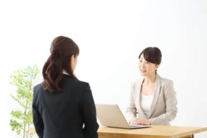 机に向かい合わせに座り、話をしているスーツ姿の2人の女性